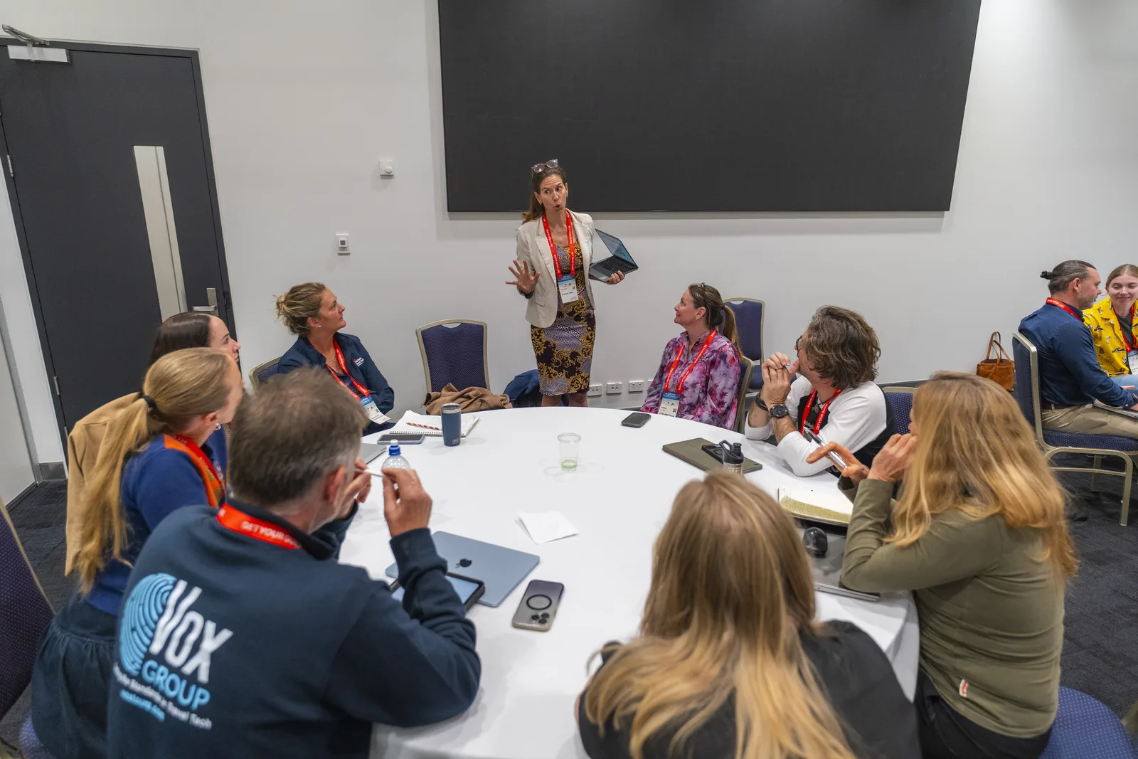 Fabienne leading a hands-on Build an AI Brain session in the Arival AI Labs, laptop in hand, a full table of operators around her